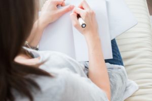 woman in white tee shirt writing with pen in notebook