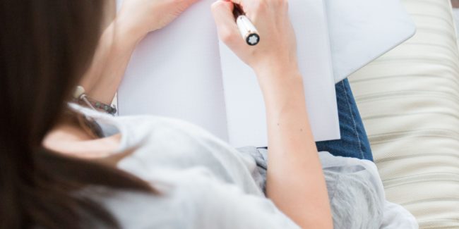 woman in white tee shirt writing with pen in notebook