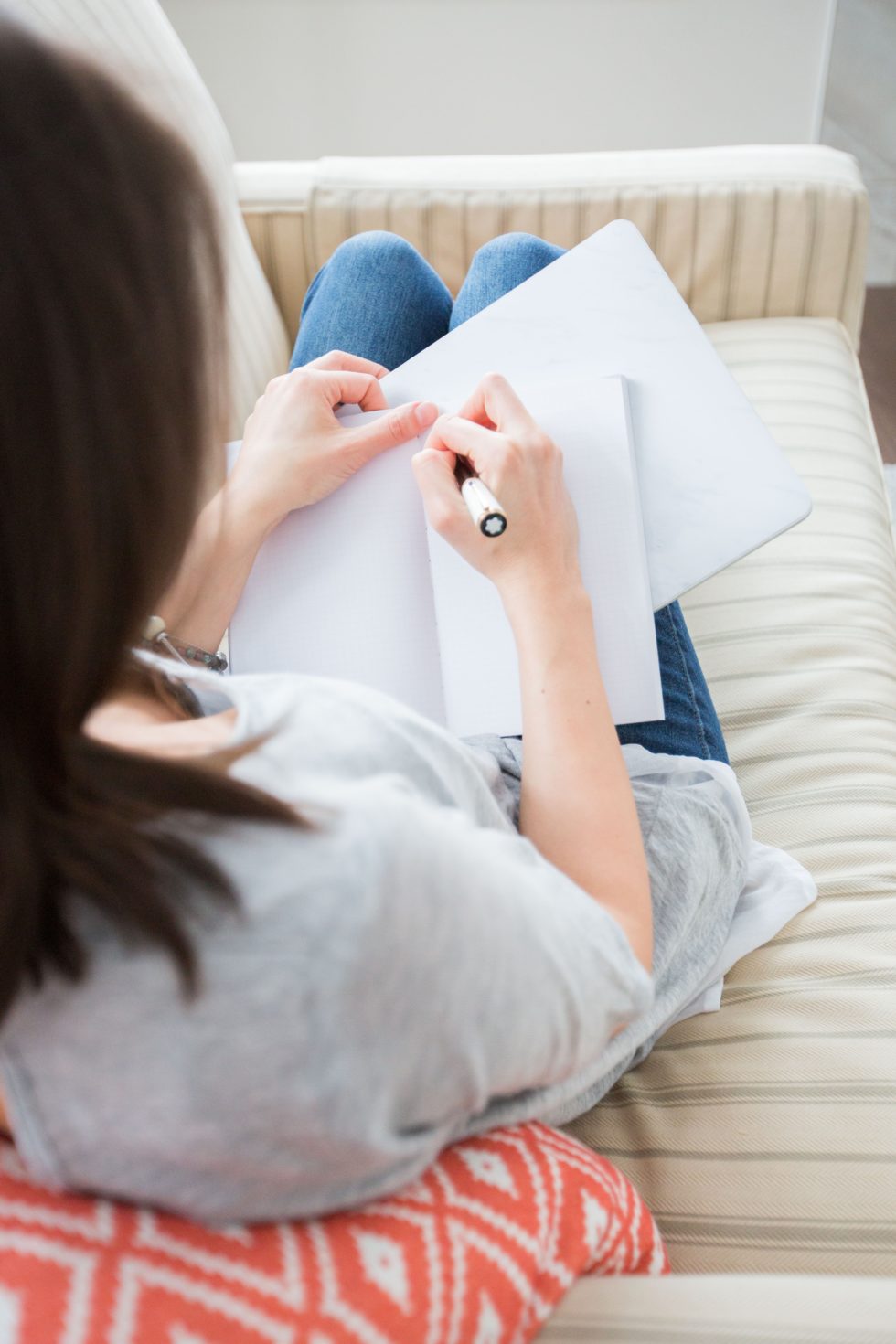 woman in white tee shirt writing with pen in notebook